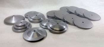 Examples of Fabricor Product’s Canopy, Can & Cover shapes for covering junction boxes or mounting hardware are arranged on a light surface. Some discs have stepped features, while others are flat and uniform.